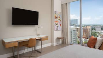 A modern hotel room with a large bed, a desk with a chair, a flat-screen TV, and a large window offering a city view.