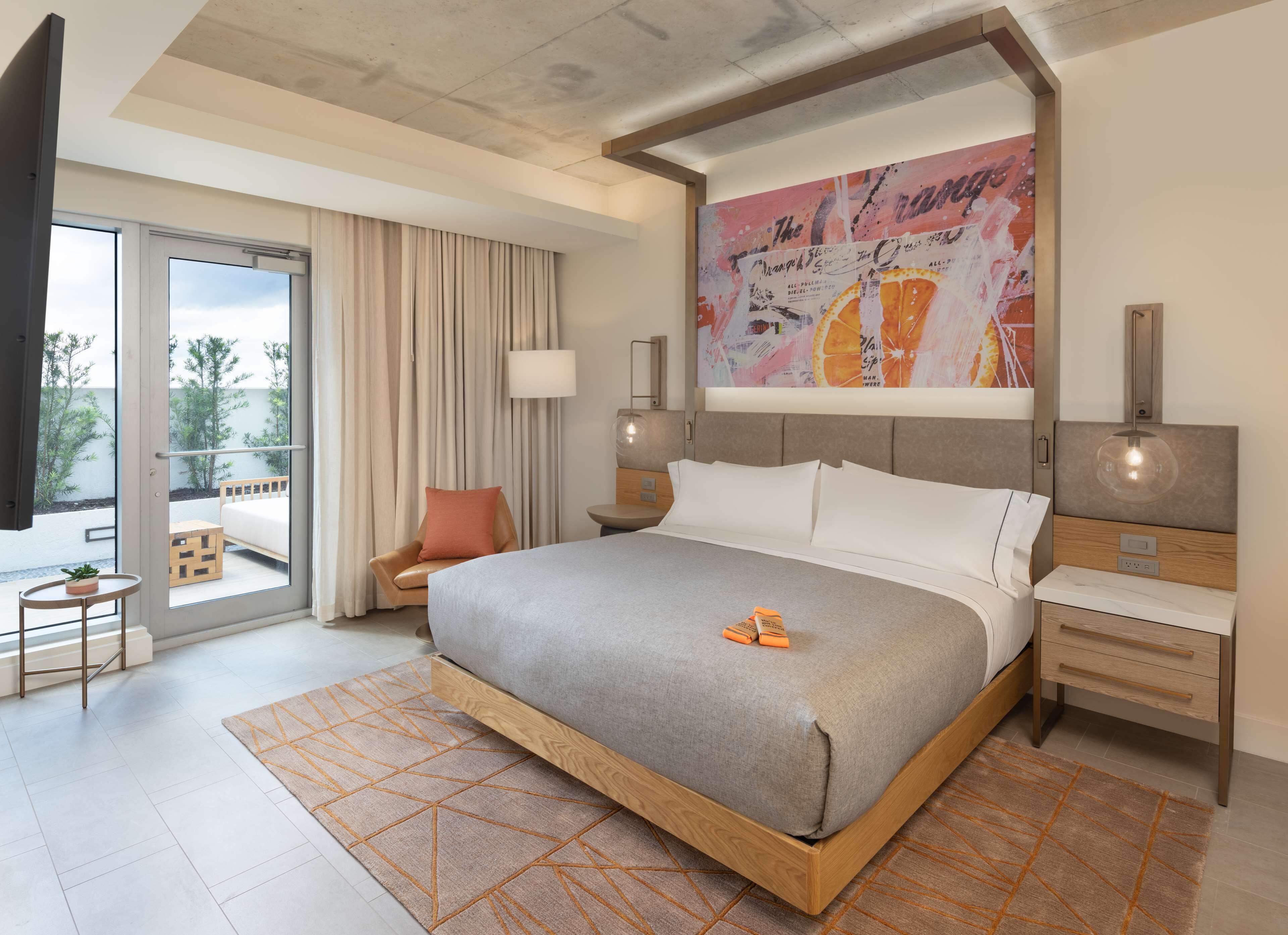 A modern hotel room with a large bed, a balcony with a view, a desk, and a painting on the wall.