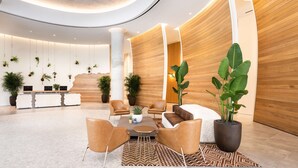 Eine moderne Lobby mit gewölbter Decke, einem Holzerreptionsschalter, einer Sitzecke mit Ledersesseln und Topfpflanzen.