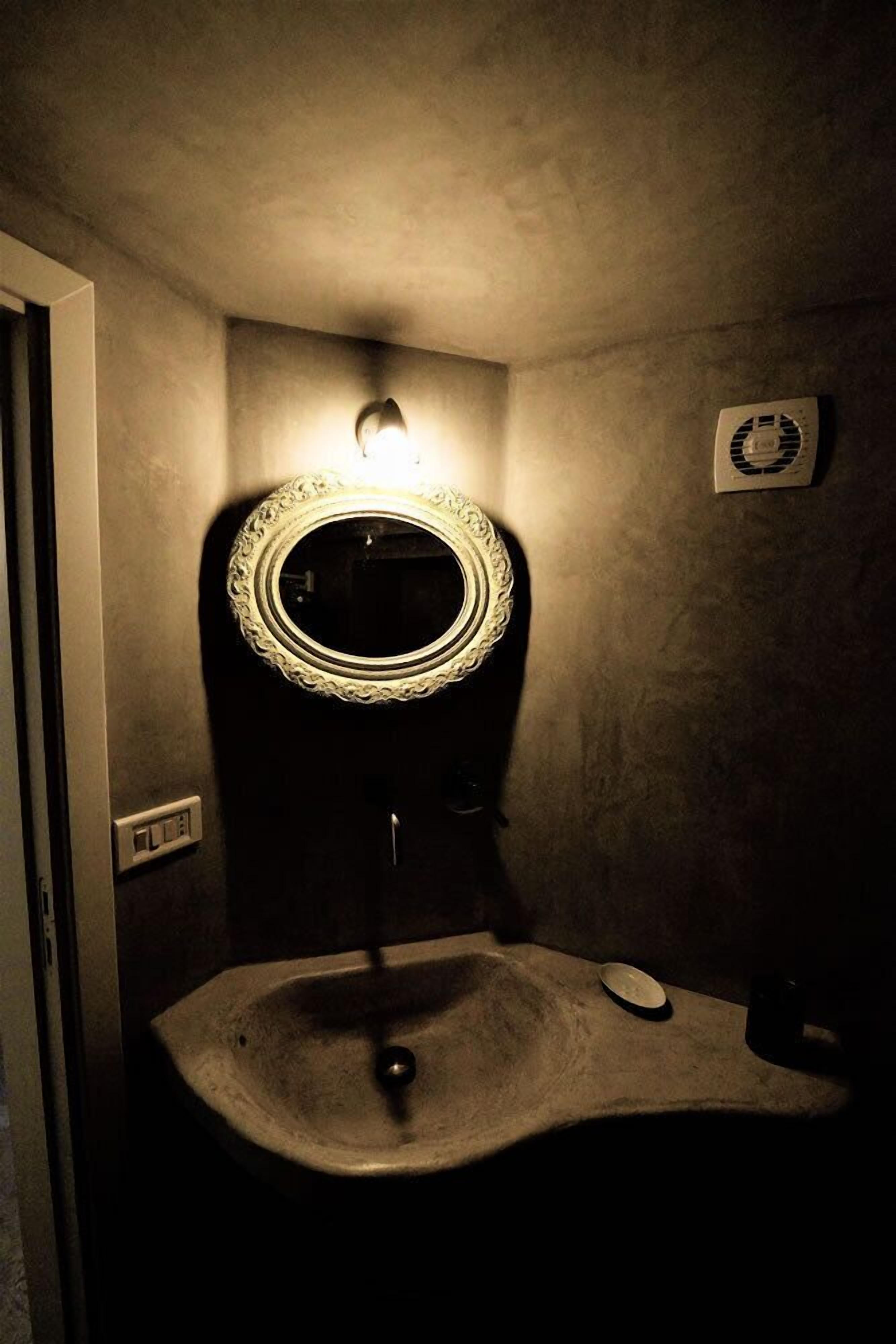 A bathroom with a round mirror, a wall-mounted light, and a ventilation fan.