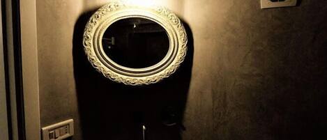 A bathroom with a round mirror, a wall-mounted light, and a ventilation fan.