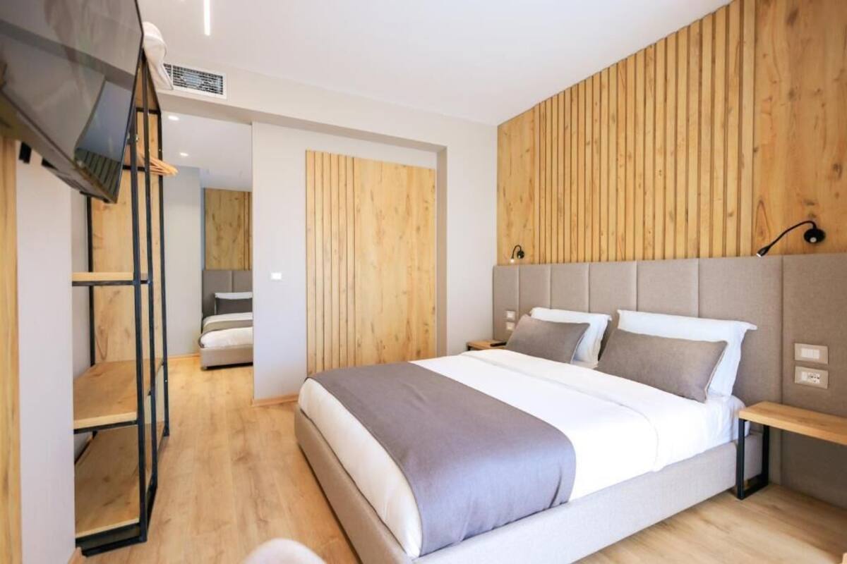 A modern bedroom with a large bed, wooden panel wall, and a TV mounted on the wall.