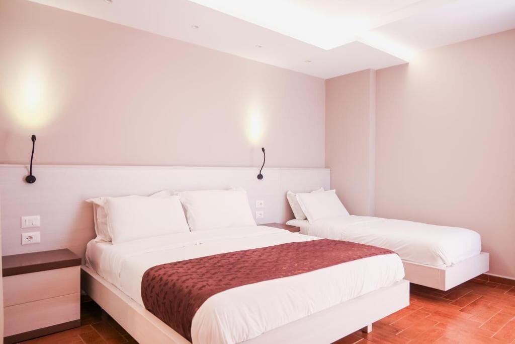 A hotel room with a large bed, a bedside table, and two wall-mounted lights.