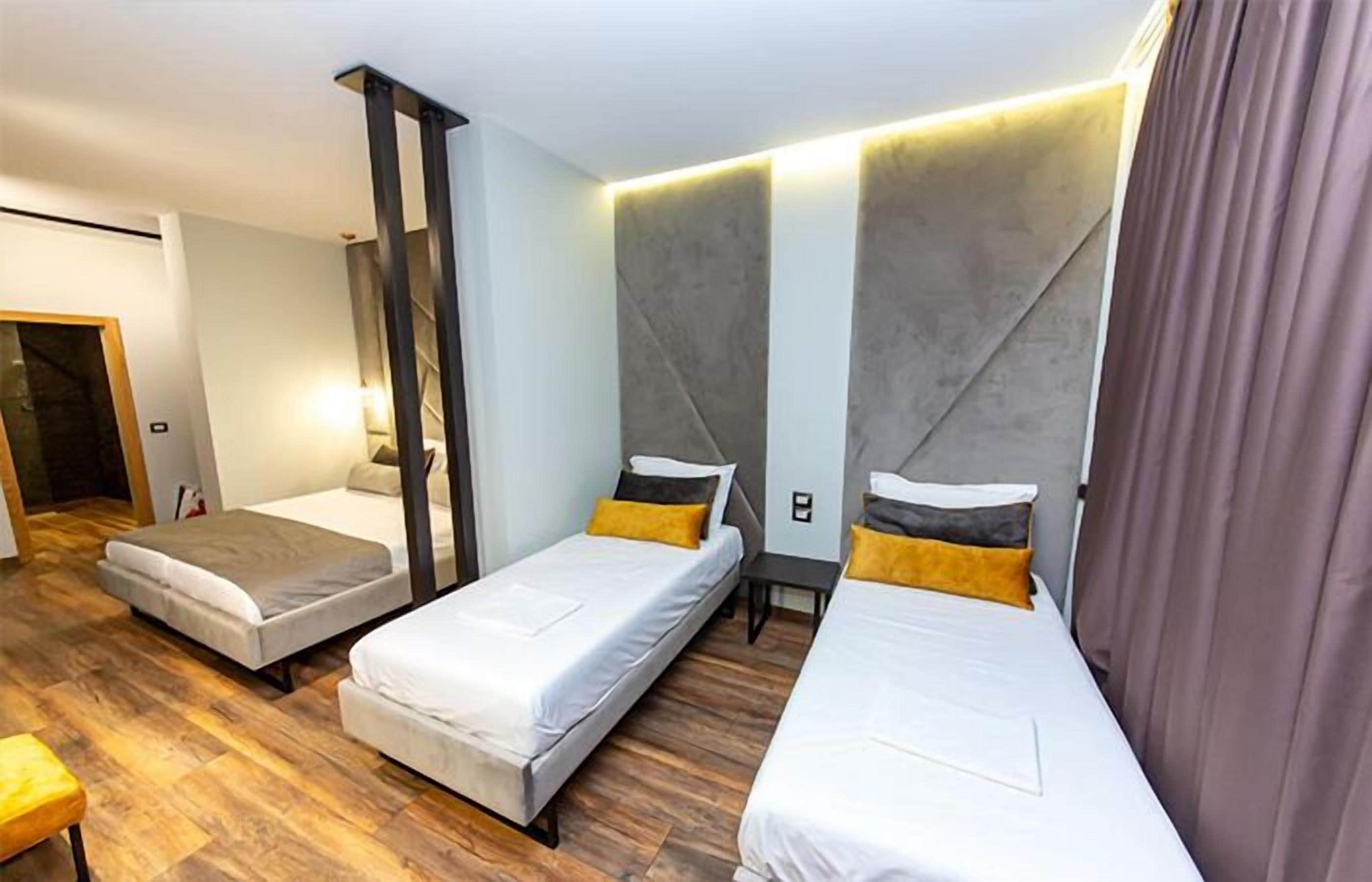A hotel room with three single beds, a wooden floor, and a modern design with a large wall panel and a light fixture.