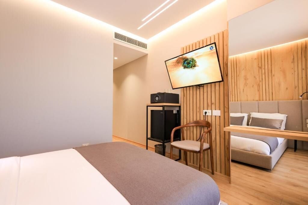 Una habitación de hotel moderna con cama, televisor montado en la pared, un armario de madera y una zona de estar con sofá.