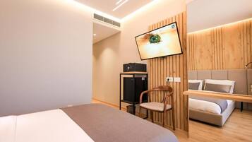 Una habitación de hotel moderna con cama, televisor montado en la pared, un armario de madera y una zona de estar con sofá.