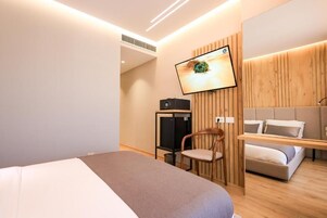 Una habitación de hotel moderna con cama, televisor montado en la pared, un armario de madera y una zona de estar con sofá.