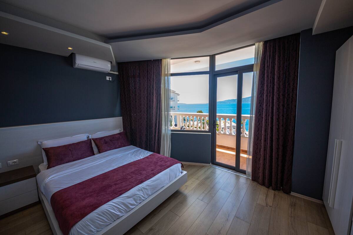 A bedroom with a bed, a window, and a view of the sea.