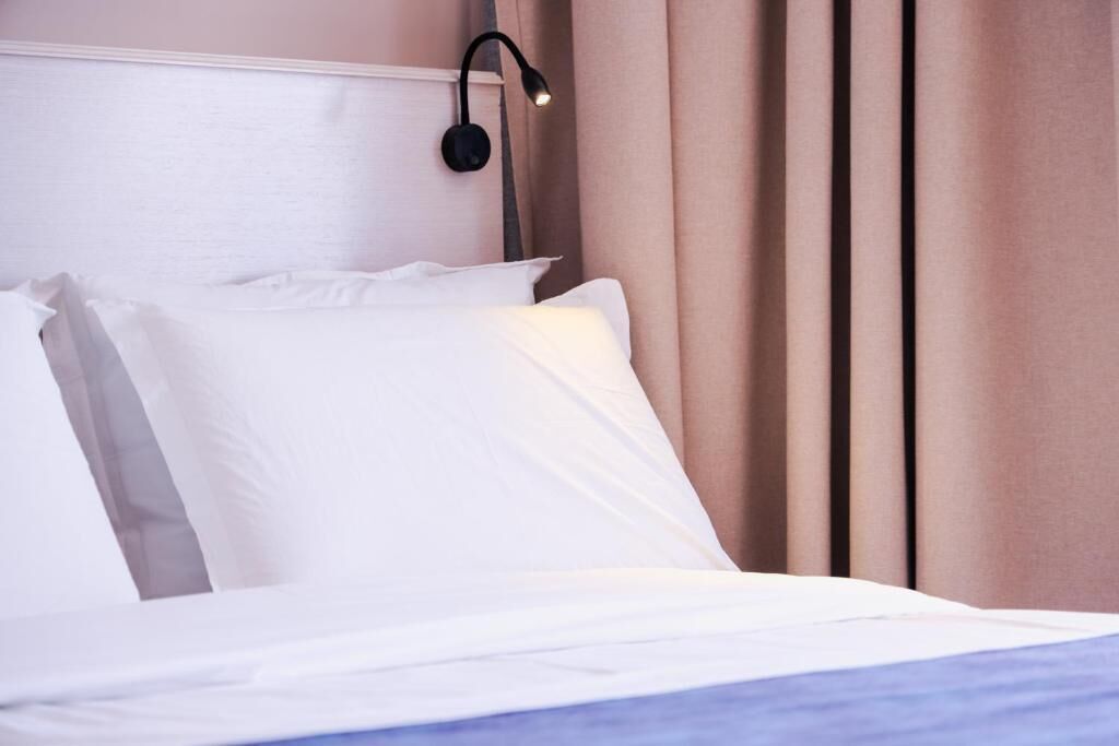 A neatly made bed with white linens and a headboard with a black wall-mounted lamp.
