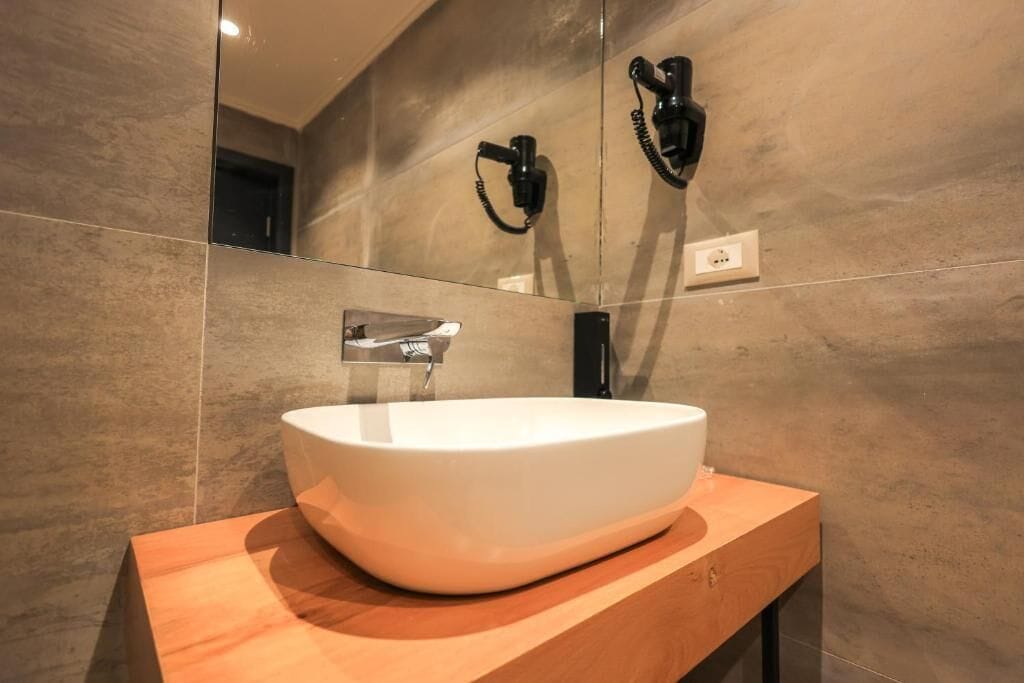 Un bagno moderno con un lavandino bianco ampio su una cassettiera in legno, uno specchio e un asciugacapelli montato a parete.