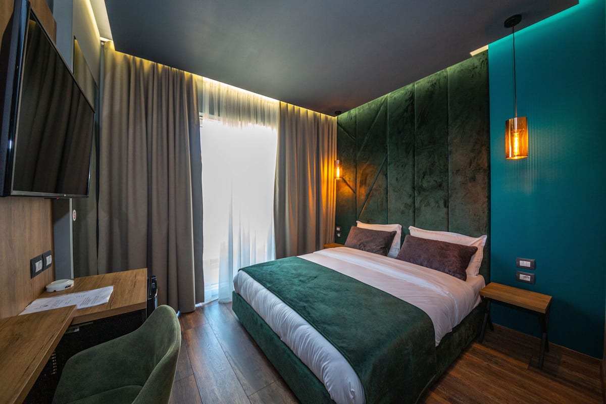A modern hotel room with a large bed, a desk with papers, a chair, and a TV.