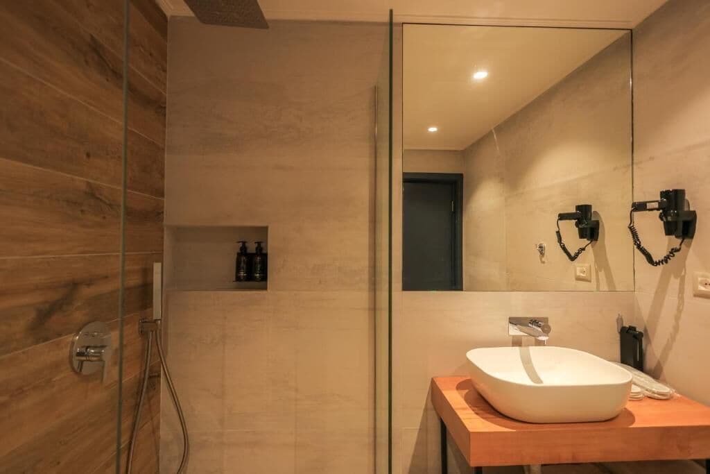 A modern bathroom with a glass shower enclosure, a wooden vanity with a white sink, and a large mirror.