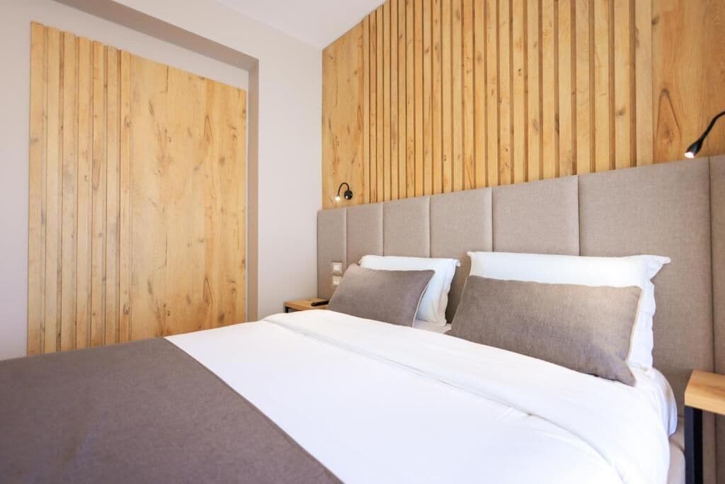 Una habitación de hotel moderna con una cama grande, paneles de madera y una mesita de noche con lámpara.