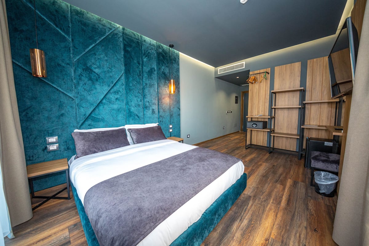 A modern bedroom with a large bed, wooden flooring, and built-in shelving.