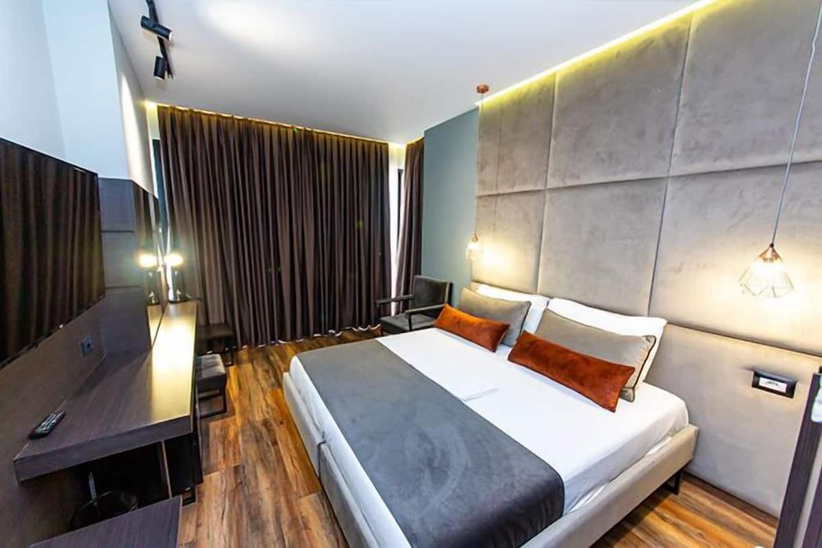 A modern hotel room with a large bed, a desk, and a TV.