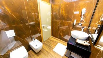A modern bathroom with a marble wall, a white toilet, a bidet, a sink, and a mirror.