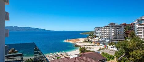 A coastal view with a beach, clear blue sea, and a mountainous backdrop.