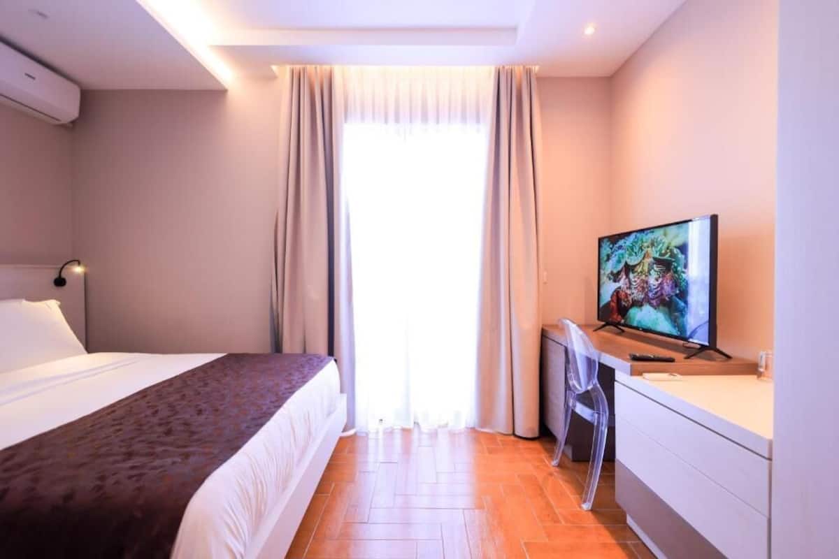 A hotel room with a bed, a desk with a chair, a television, and a window with curtains.