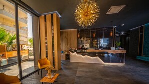 A modern reception area with a wooden reception desk, a large glass window, and a stylish pendant light. - Hotel Apollon Saranda (Sarandë)