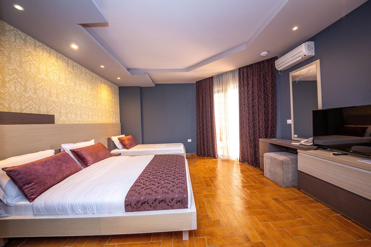 A hotel room with two beds, a TV, a desk, and an air conditioning unit.