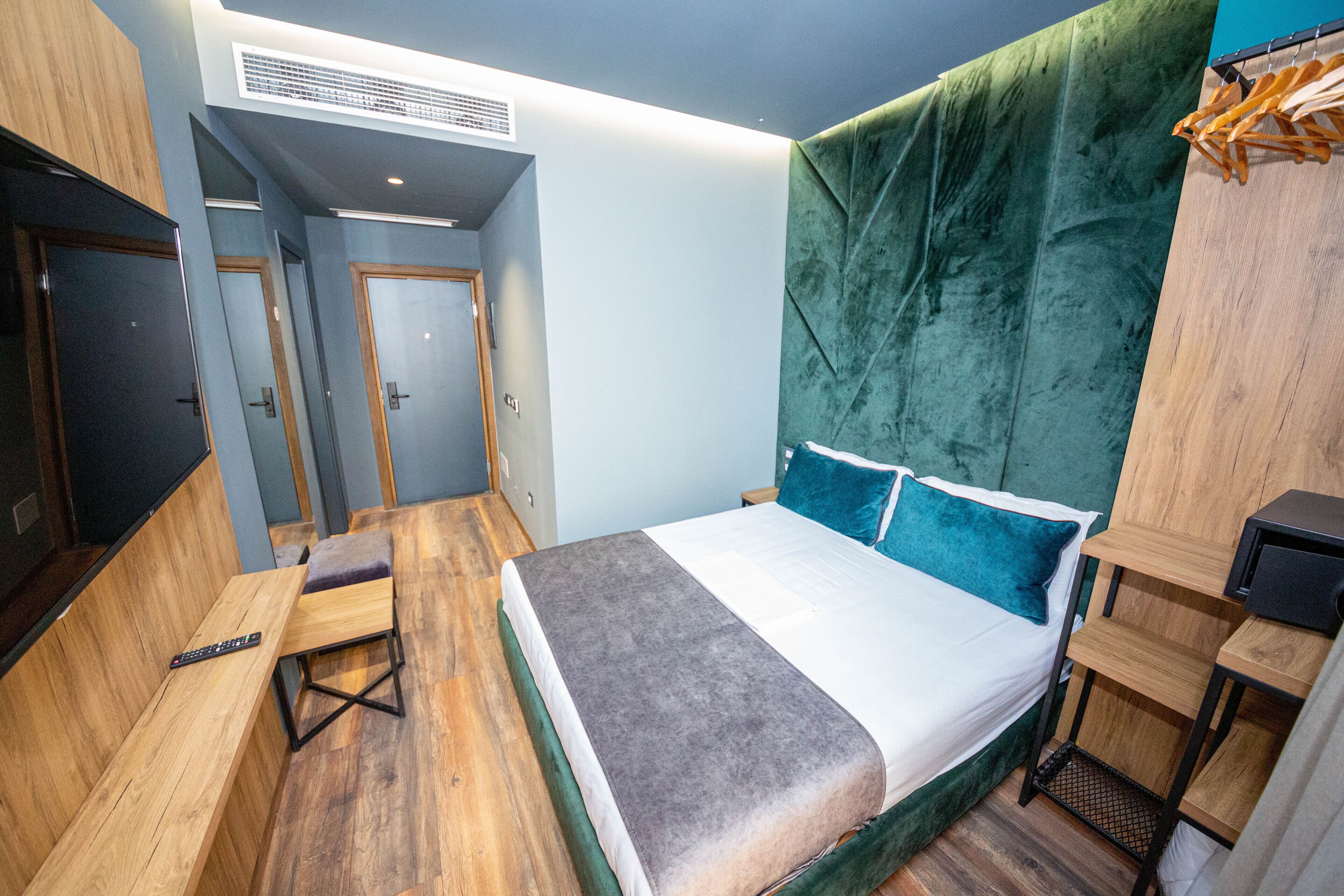 Een kleine hotelkamer met een bed, een bankje, een tafeltje en een kledingkast.