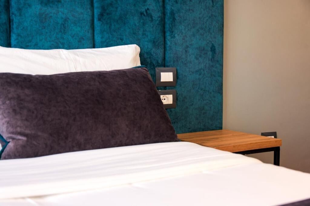 A bed with white and dark grey pillows, a wooden nightstand, and a teal upholstered headboard.