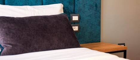 A bed with white and dark grey pillows, a wooden nightstand, and a teal upholstered headboard.