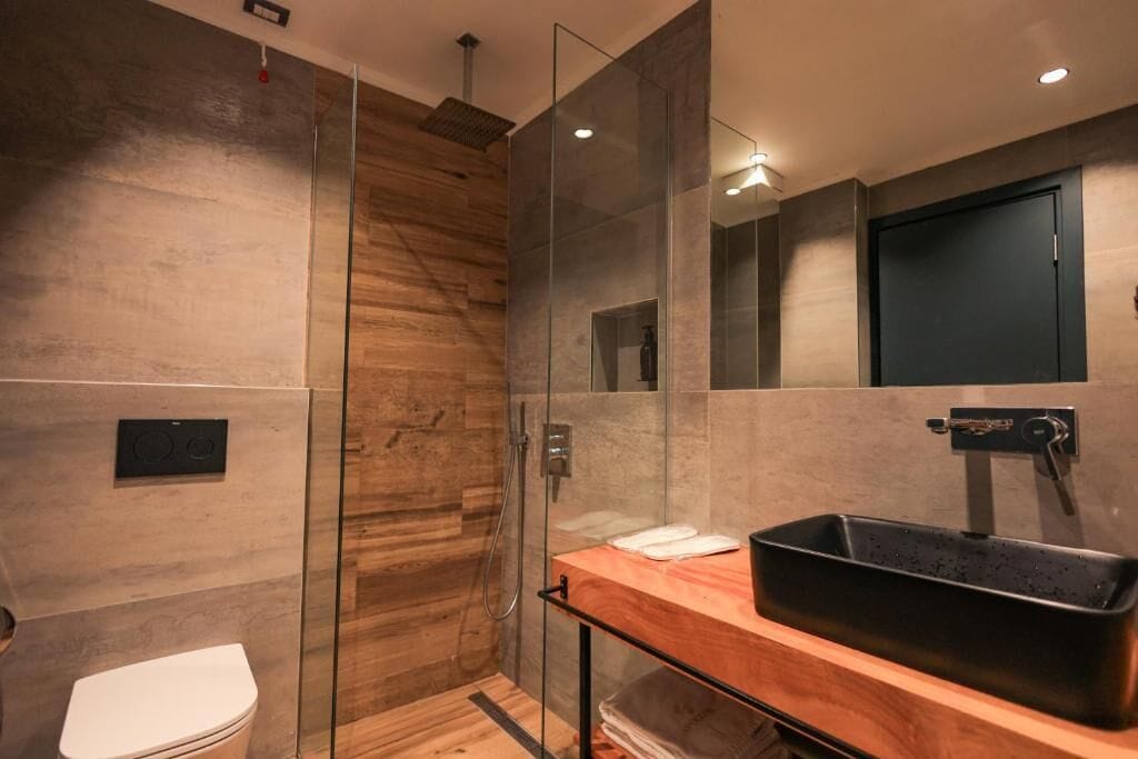 Een moderne badkamer met een glazen douchecabine, een houten wastafelmeubel en een zwarte wasbak.