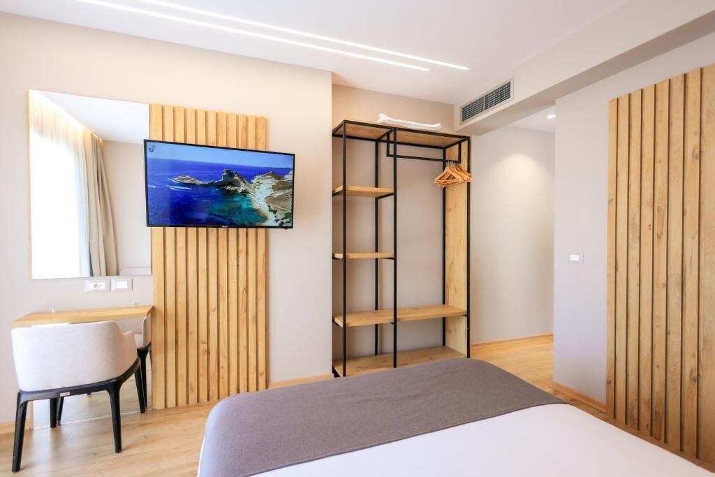A modern bedroom with a bed, a desk, a TV, and a wooden wardrobe.
