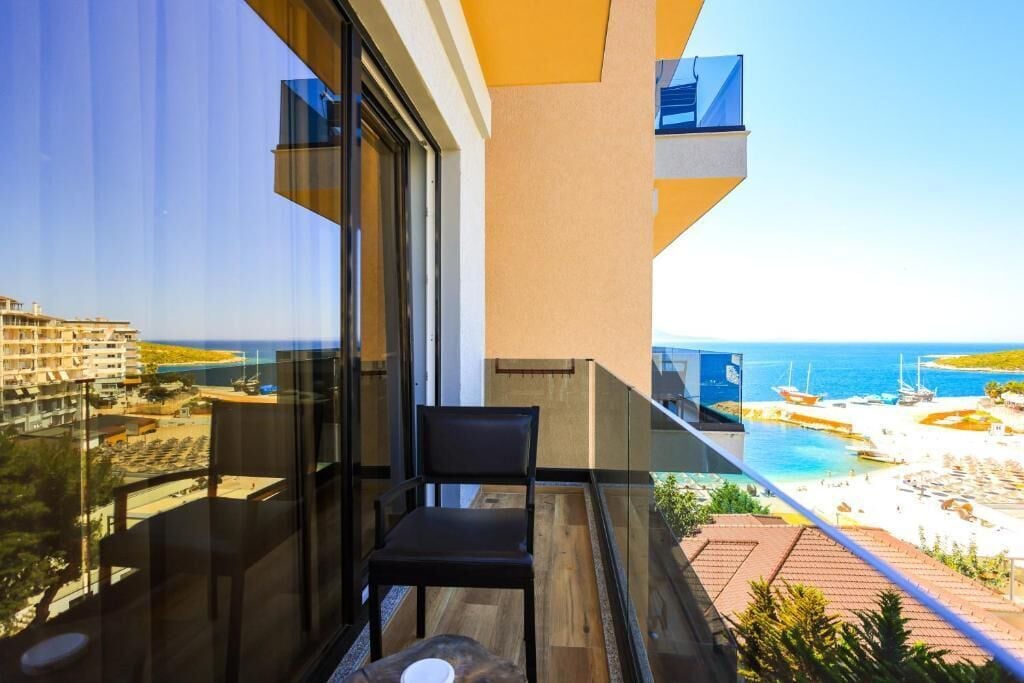 A balcony with a clear view of a beach and ocean, a chair, and a table.
