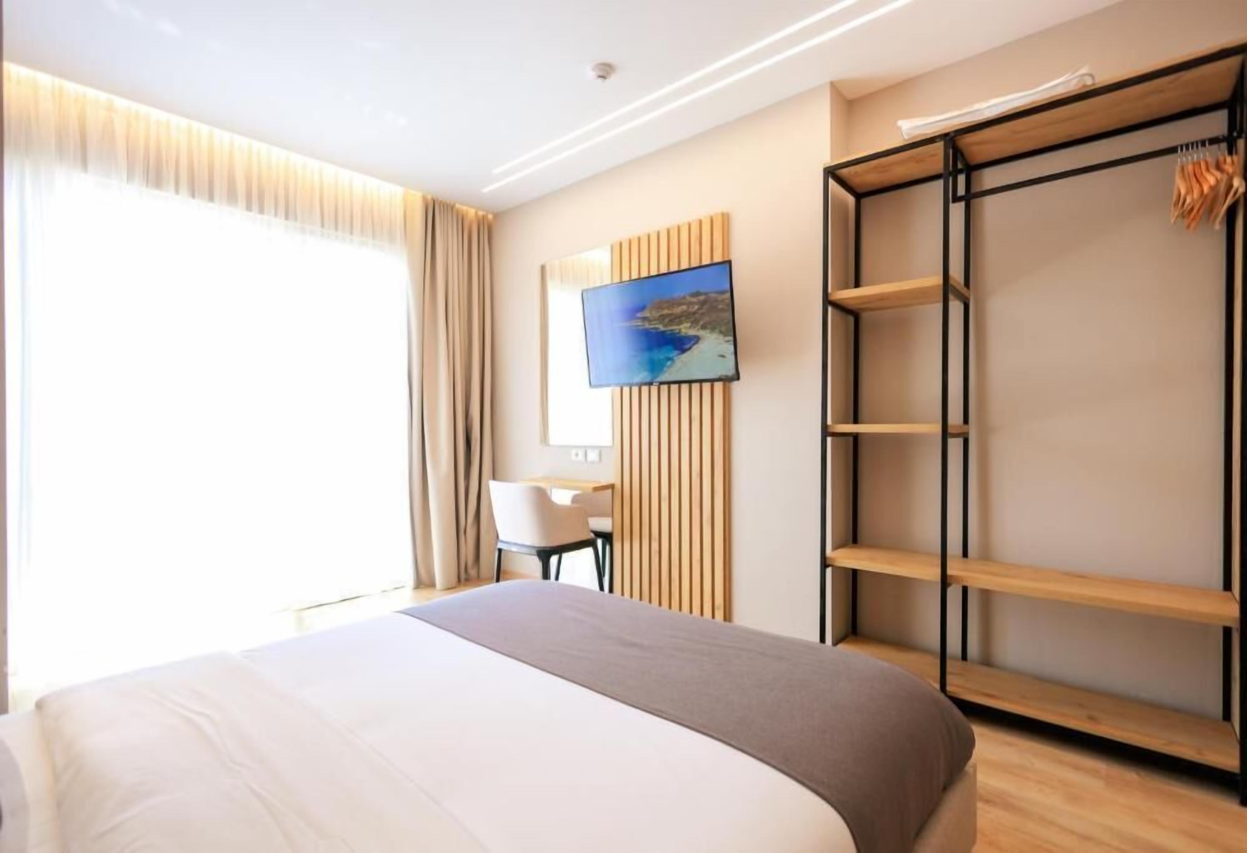 A hotel room with a bed, a desk, a TV mounted on the wall, and a wardrobe with shelves.
