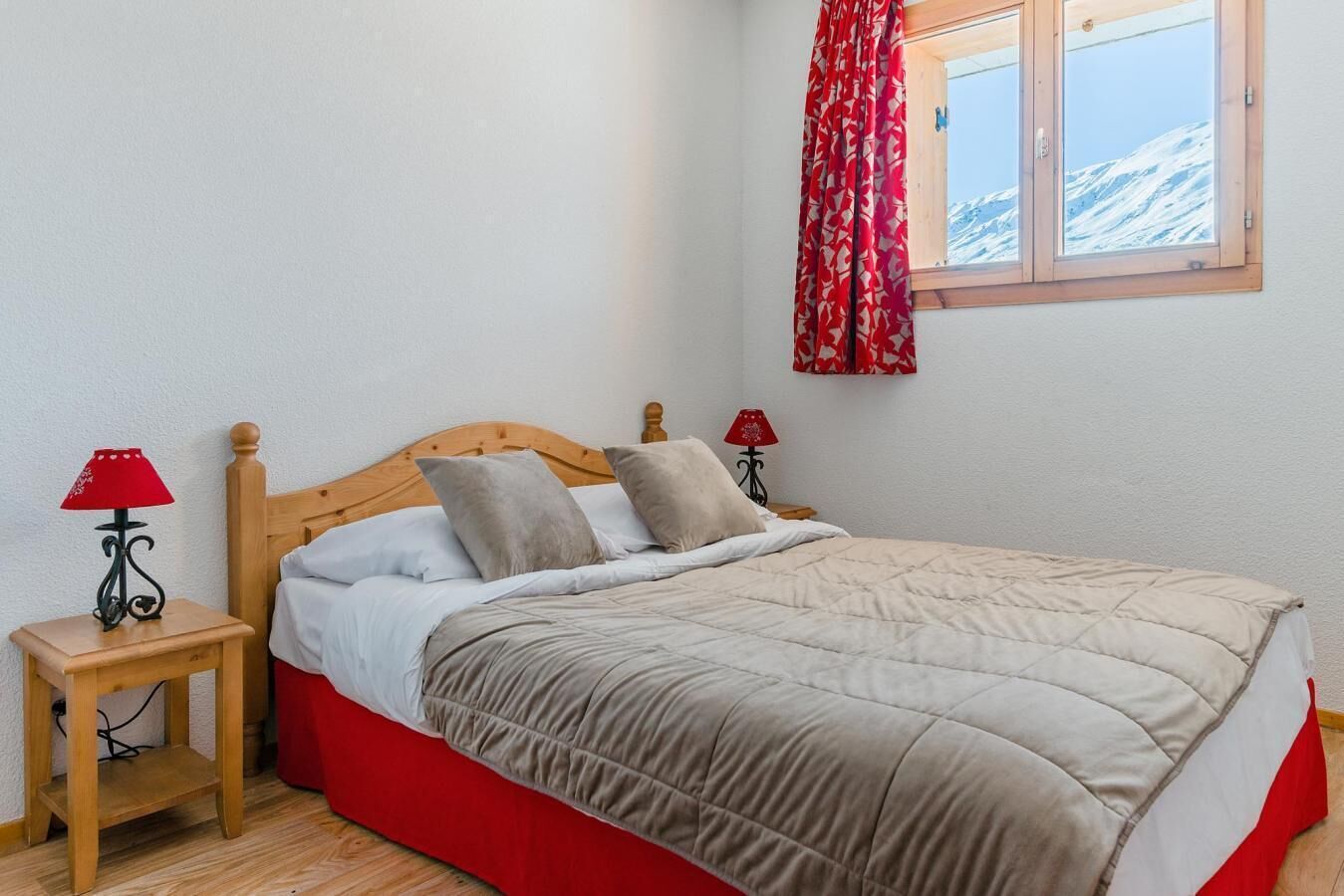 Ein Schlafzimmer mit einem hölzernen Bett, zwei Nachttischen mit Lampen, einem Fenster mit Blick auf schneebedeckte Berge und einem roten Vorhang.