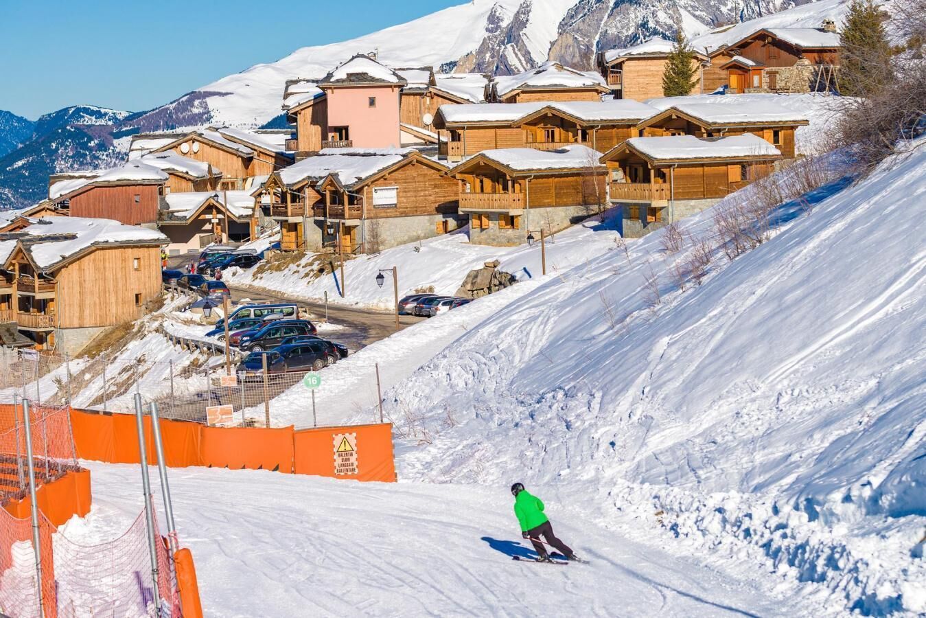 A ski resort with wooden cabins, a ski slope, and a person skiing.