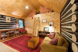 Living room w sleeping loft above, games/DVDs on the shelf at left.
