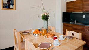 A dining table set with breakfast items, a vase with flowers, and a kitchen in the background.