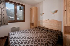 A bedroom with a bed, a window with a view of mountains, a radiator, and wooden furniture. - 100m from shops, swimming pool, terrace, balcony, tv, 38m², Les Saisies (Hauteluce)
