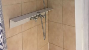 Une douche équipée d’un pommeau de douche à main et d’un robinet fixé au mur.