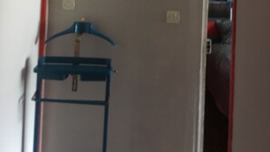 Un couloir avec une affiche encadrée accrochée au mur, un cintre bleu et un chambranle de porte rouge et blanc.
