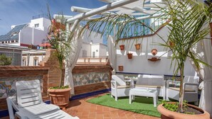 Una terraza con mobiliario de mimbre blanco, macetas de terracota y suelo de baldosas.