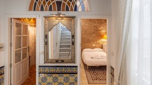 Un dormitorio con cama, mesita de noche, lámpara, espejo decorativo y suelo de baldosas.