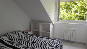 A bedroom with a bed, a window with a view of greenery, a radiator, and built-in shelving.
