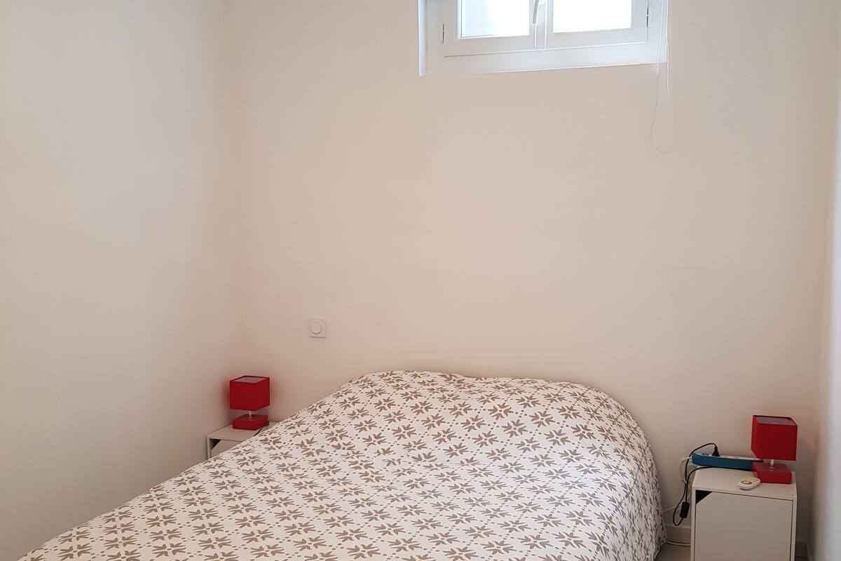 A bedroom with a bed, two bedside tables with lamps, a window, and a small window blind.