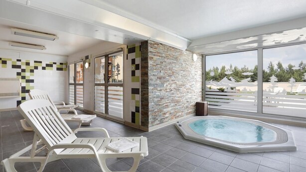 A modern indoor pool area with lounge chairs, a stone wall, and large windows offering a view of the outdoors. - Wifi, 100m from resort center, fitness, swimming pool, terrace, balcony, tv, ski locker, 41m² (Pyrénées 2000)