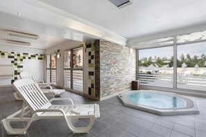 Uma área de piscina interna moderna, com espreguiçadeiras, uma parede de pedra e vista para um bairro residencial.