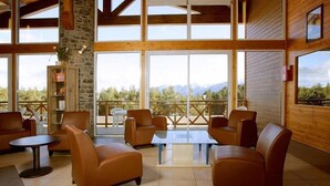 A spacious indoor area with leather sofas, a coffee table, and a stone pillar. Large windows offer a view of mountains. - Wifi, 100m from resort center, fitness, swimming pool, terrace, balcony, tv, ski locker, 41m² (Pyrénées 2000)