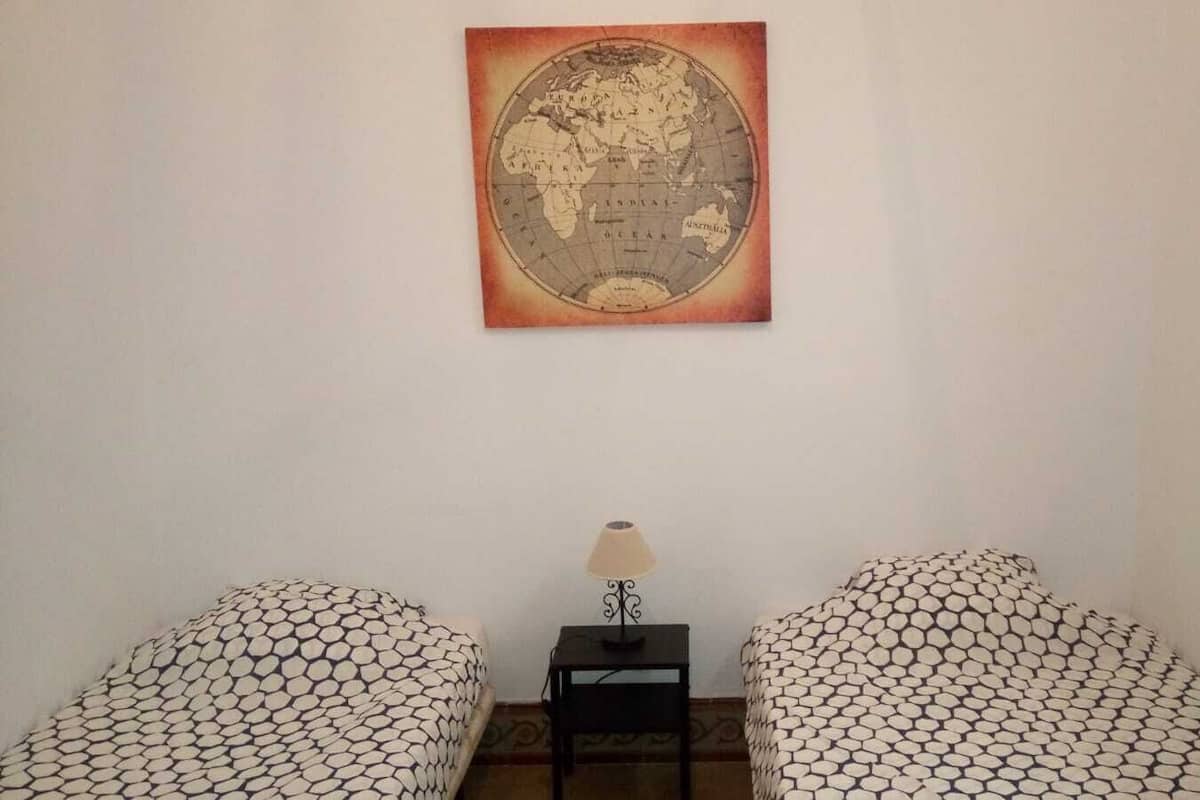 Una habitación con dos sillones estampados, una mesita con una lámpara y un mapa antiguo en la pared.