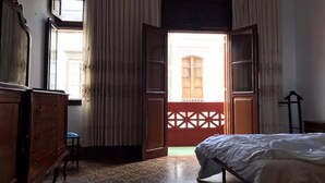 Una habitación con cama, cómoda de madera y ventana con cortinas.
