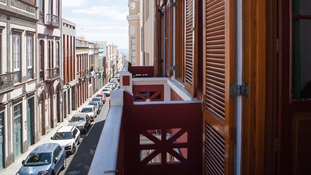 Una calle estrecha bordeada de edificios, con balcones y una fila de coches aparcados.