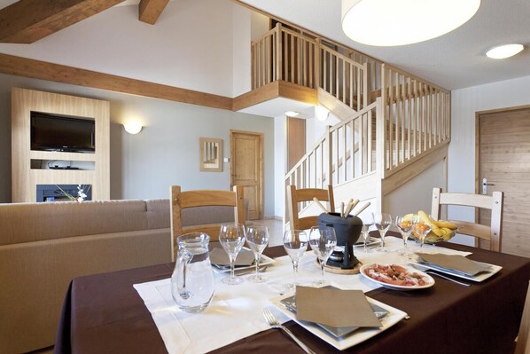 Un coin repas avec une table dressée pour deux personnes, des chaises en bois, un lustre et un escalier avec des rampes en bois.