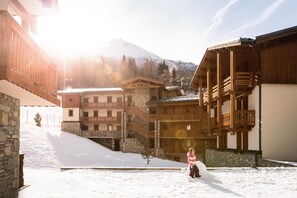 A snow-covered courtyard with wooden buildings, stone walls, and a mountain in the background. - Wifi, 200m from ski slopes, fitness, swimming pool, sauna, hammam, balcony, tv, ski locker, 35m² (Lanslevillard)